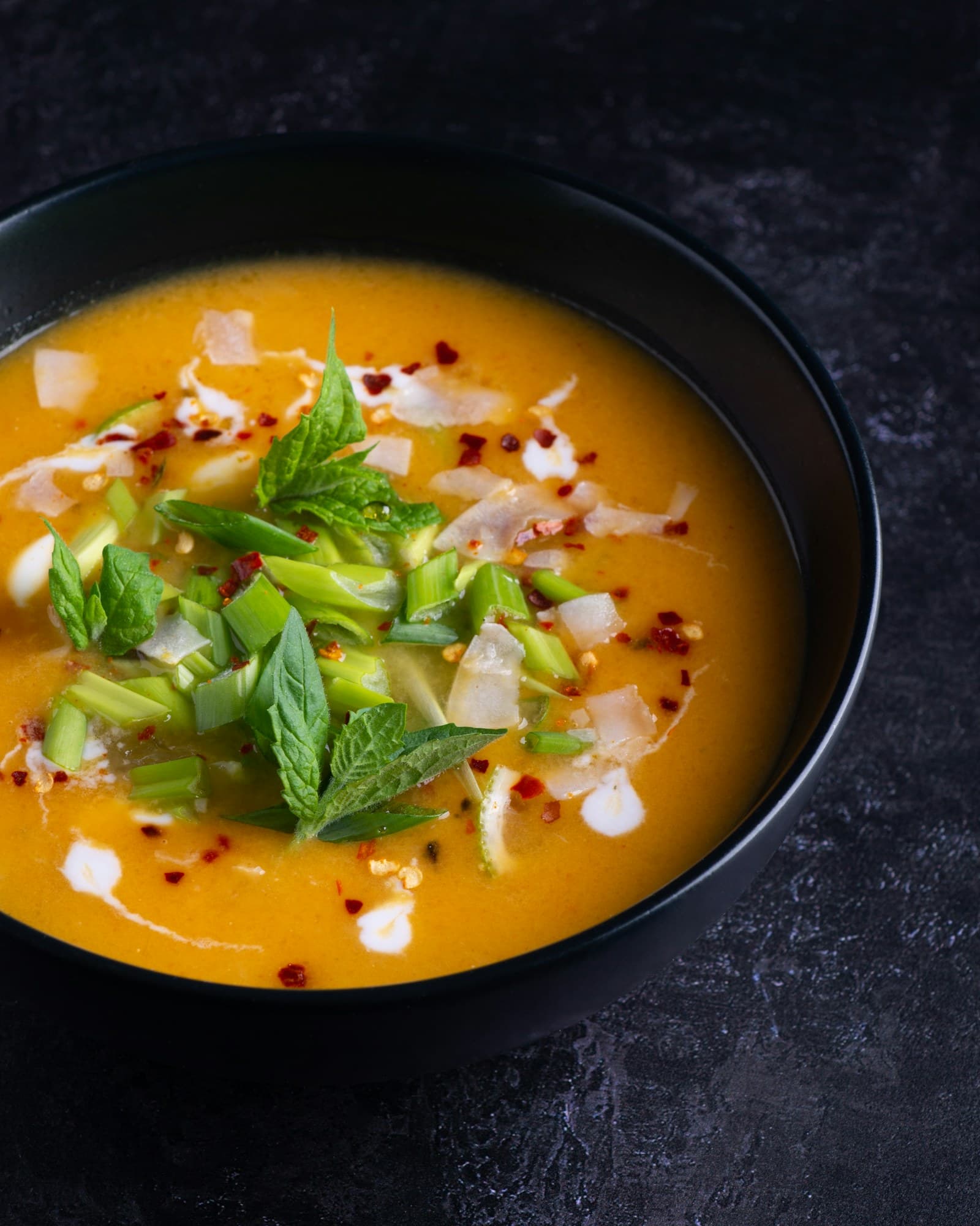 A golden squash soup topped with fresh herbs and cream